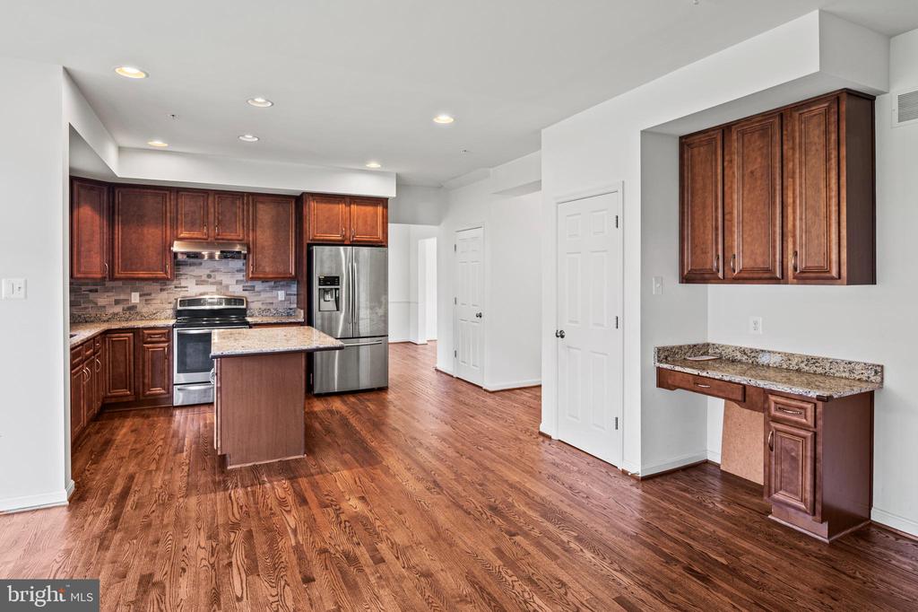 Kitchen with dark wood cabinets, a granite-topped island, stainless steel appliances, and hardwood flooring.