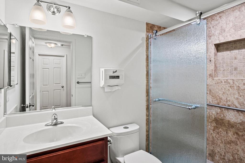 Bathroom with a dark wood vanity and a glass shower featuring pink-brown tile and a recessed niche.