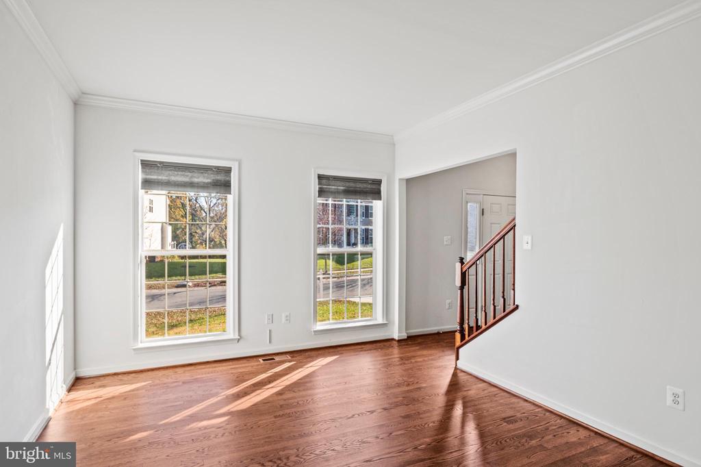 Vacant living room with polished hardwood floors, two tall windows, and a staircase.