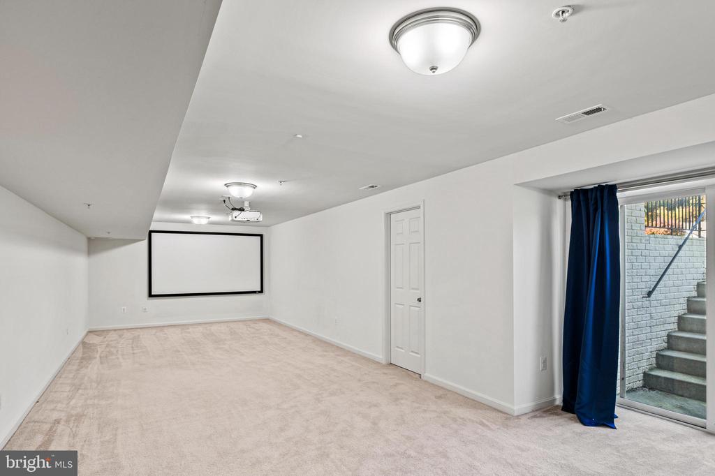 Empty media room with a projection screen, ceiling-mounted projector, and blue curtains by a sliding glass door.