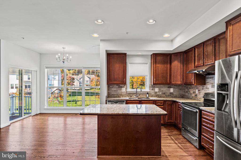 Kitchen with a large granite island, dark wood cabinets, and stainless steel appliances.