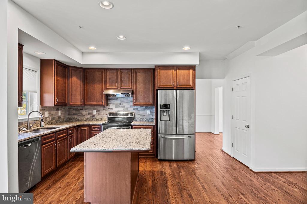 Kitchen with dark wood cabinetry, granite island, stainless steel appliances, and hardwood floors.