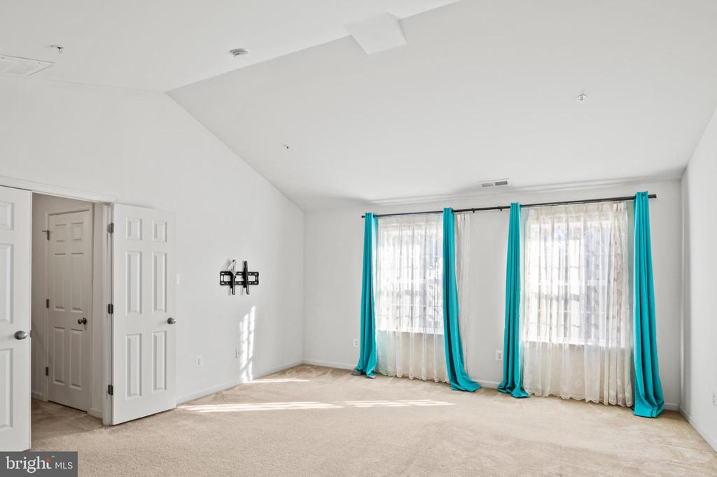 Vacant carpeted bedroom with two windows, sheer curtains, and turquoise drapes.