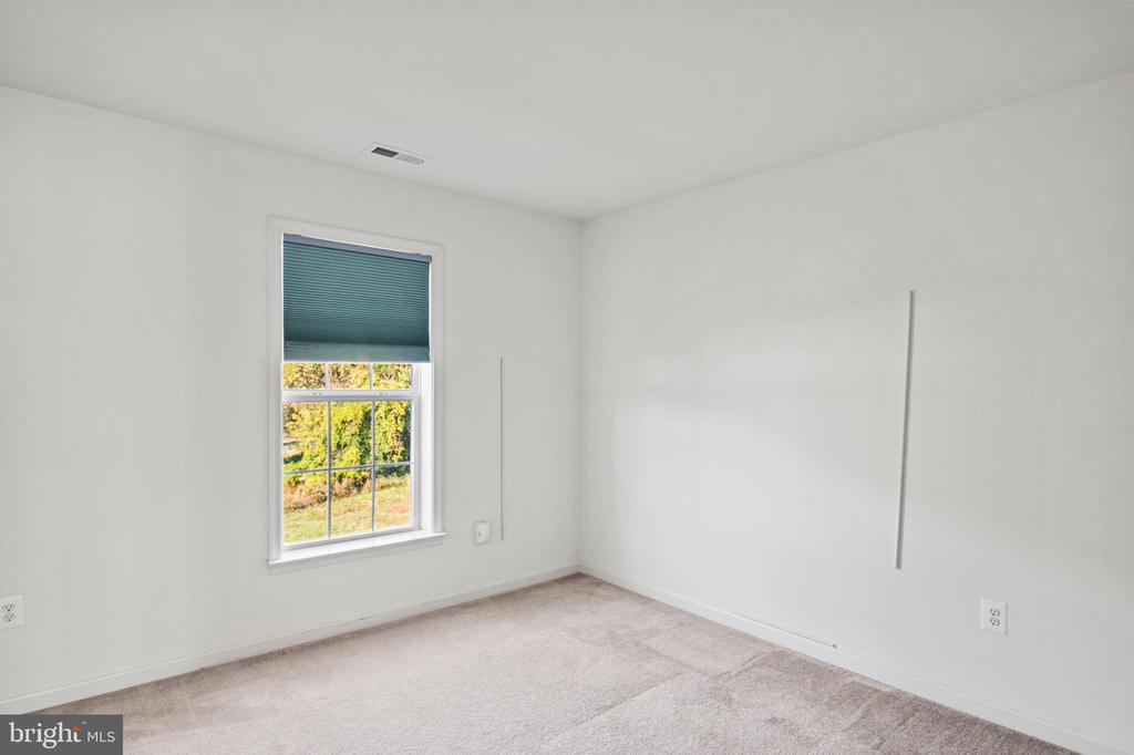 Vacant bedroom with light carpet and a window with a partially lowered teal blind.