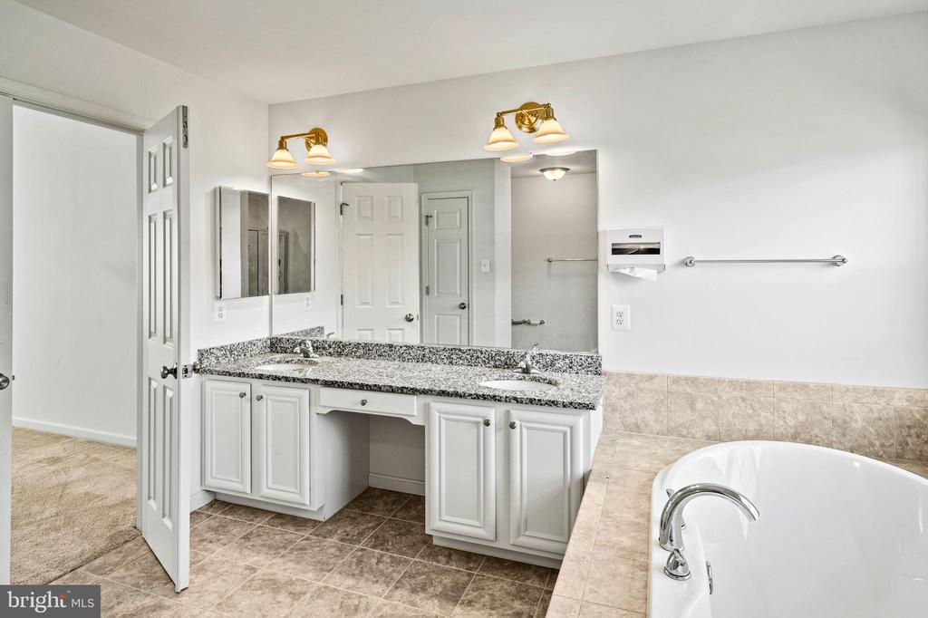 Bathroom with a white double vanity and granite counter beside a built-in soaking tub.