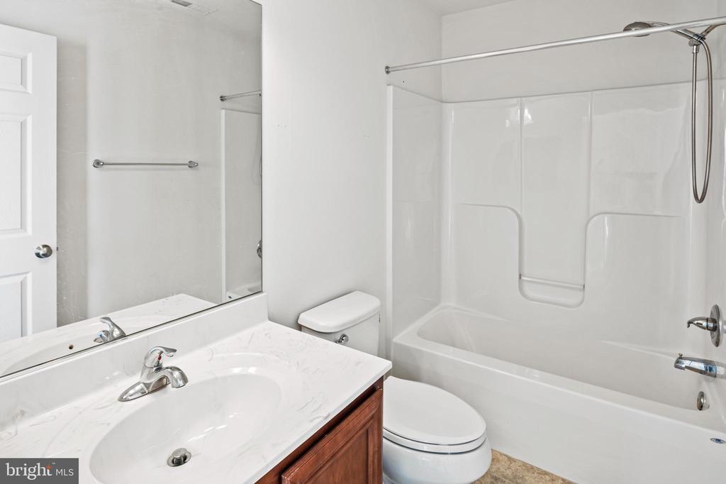 Bathroom with a white tub and shower beside a marble-look vanity and large mirror.