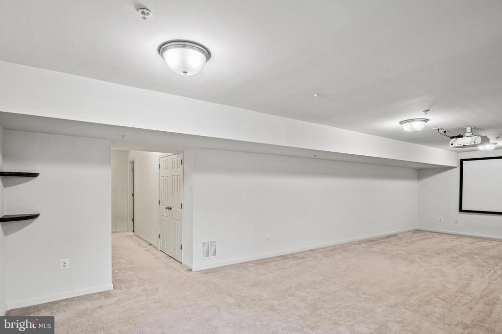 Basement recreation room with a projection screen, ceiling-mounted projector, and beige carpet.