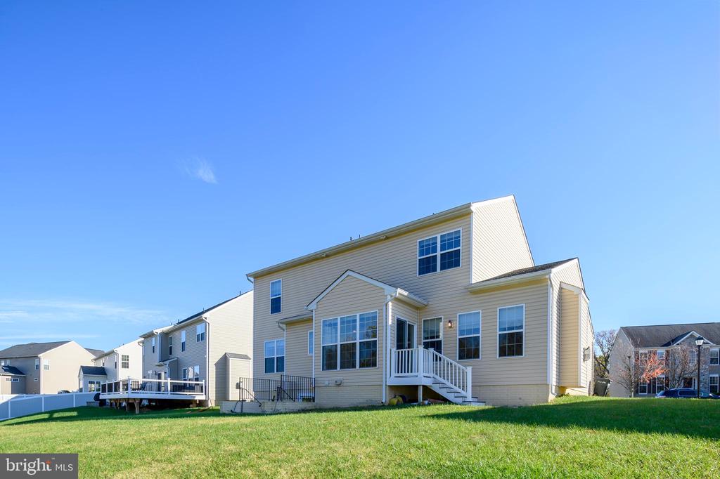 Rear of a beige two-story house with a raised deck and stairs overlooking a green lawn.