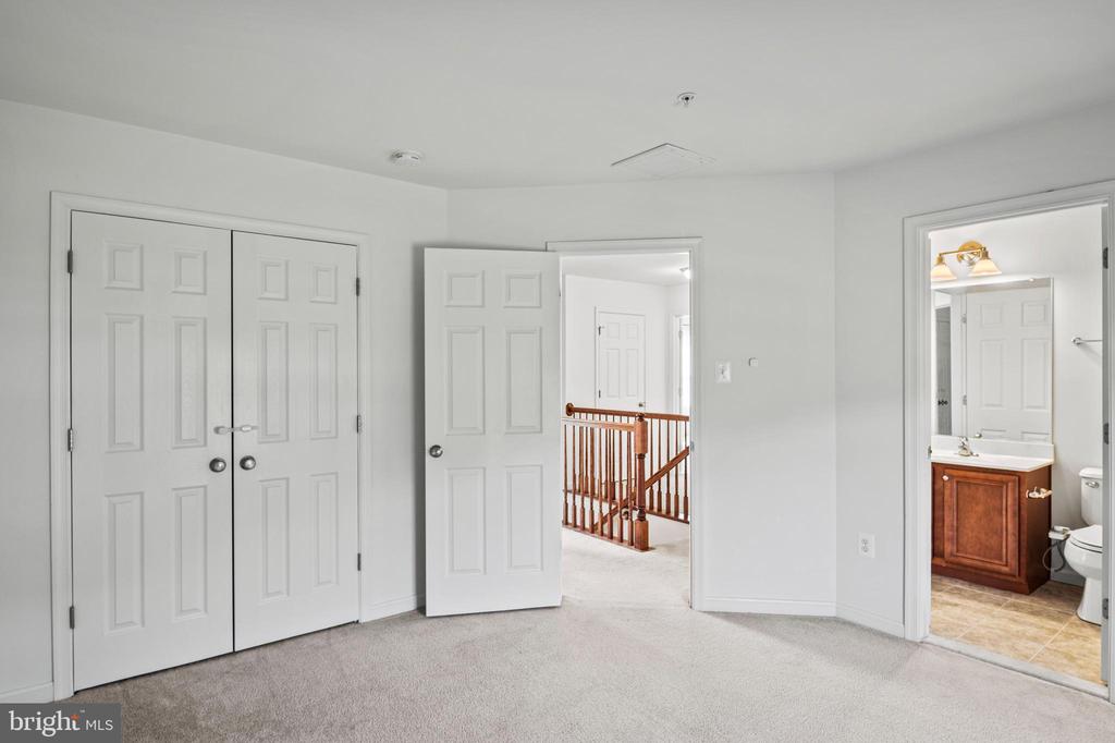 Carpeted empty bedroom with double closet doors and an open doorway to a bathroom.