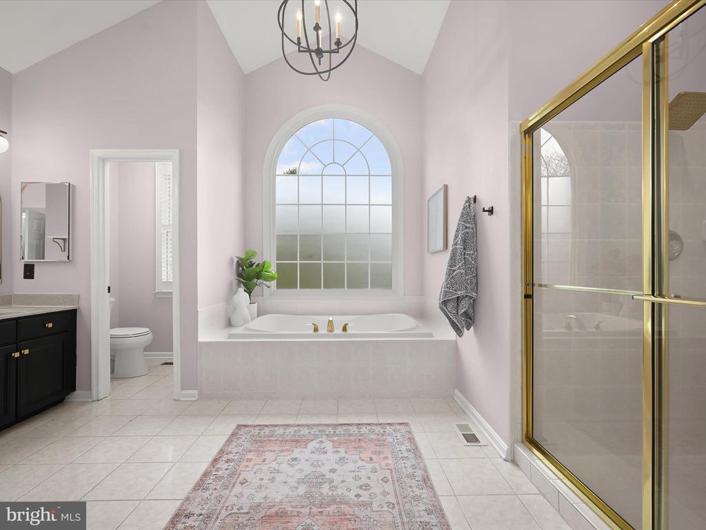 Primary bathroom with an arched window above the soaking tub and a gold-framed glass shower.