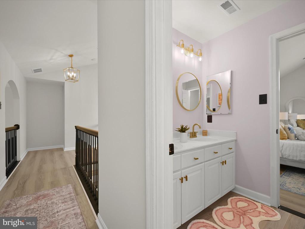 Pale pink bathroom with a white vanity and gold fixtures beside a carpeted landing with dark railings.