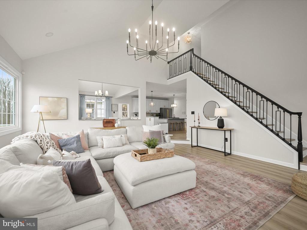 Staged living room with a white sectional, high ceiling, and black metal staircase leading to the upper floor.