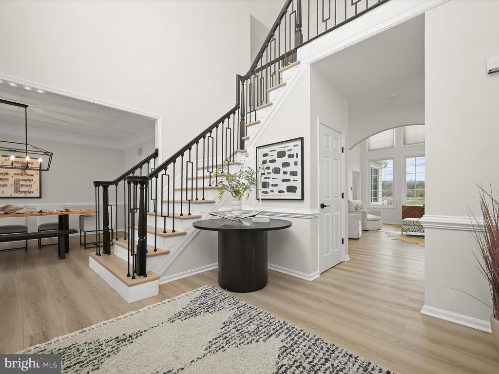 Two-story foyer with a black iron-railed staircase, round console table, and adjoining dining area.