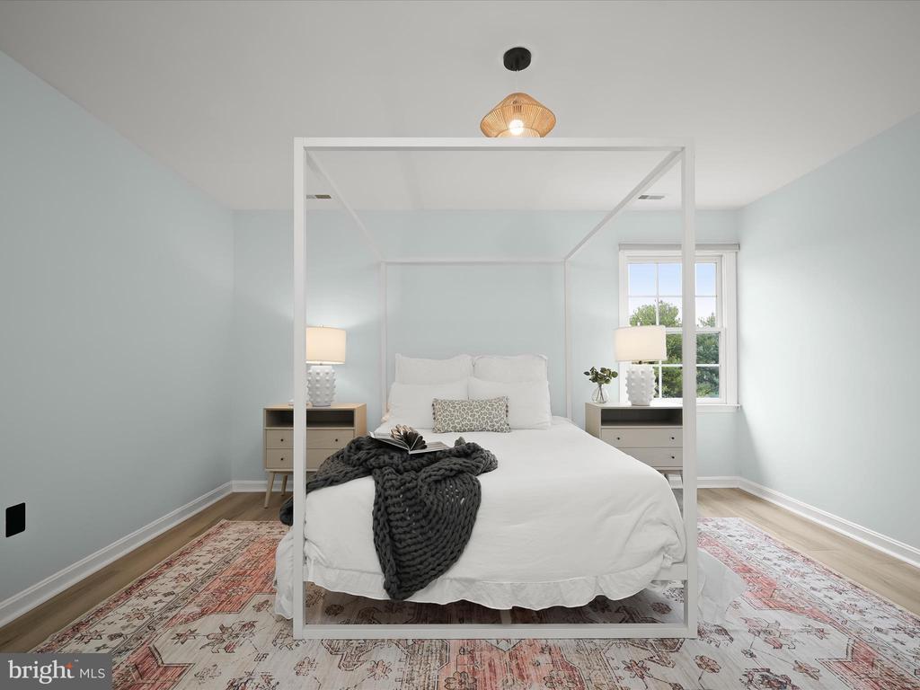 Staged bedroom with a white canopy bed, pale blue walls, and a patterned rug.