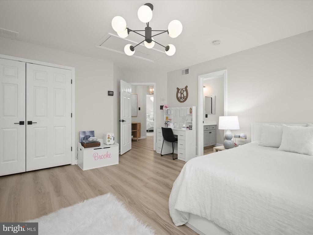 Bedroom with a white bed, wood-look floors, globe chandelier, and desk nook.