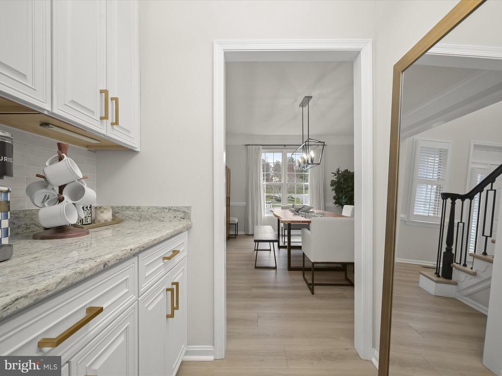Bright kitchen with white cabinets and stone counters, opening onto a furnished dining area.