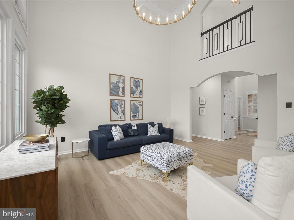 Staged living room with a navy sofa, white seating, and a dramatic double-height ceiling.