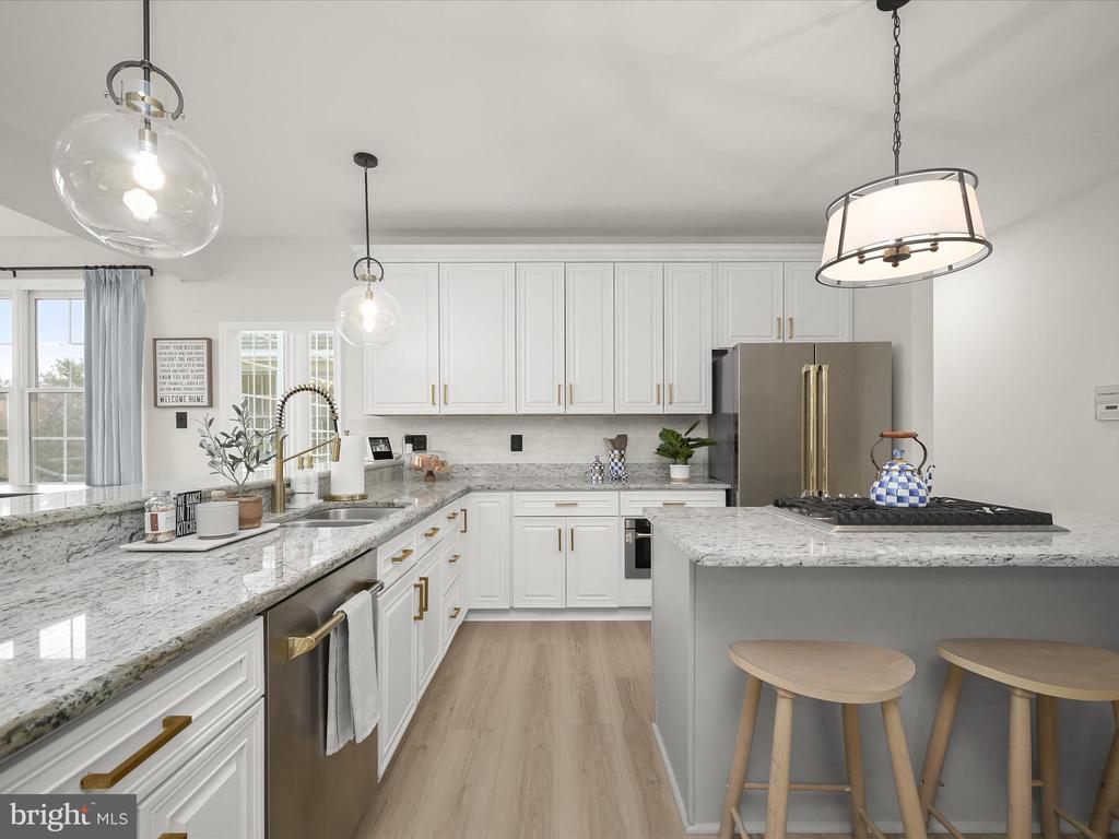 Kitchen with white cabinets, veined stone counters, a gas cooktop island, and brass hardware.