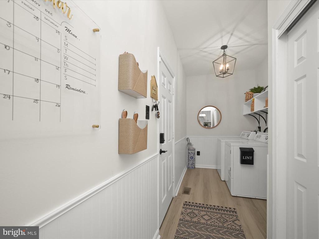 Laundry room with white washer and dryer, beadboard wainscoting, and a patterned runner.