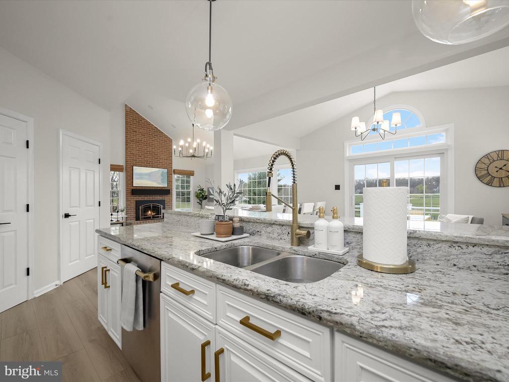 Bright kitchen with a stone island, double sink, brass fixtures, and a brick fireplace.