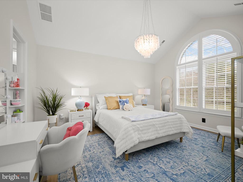 Furnished bedroom with a white bed, blue patterned rug, chandelier, and tall arched shuttered windows.