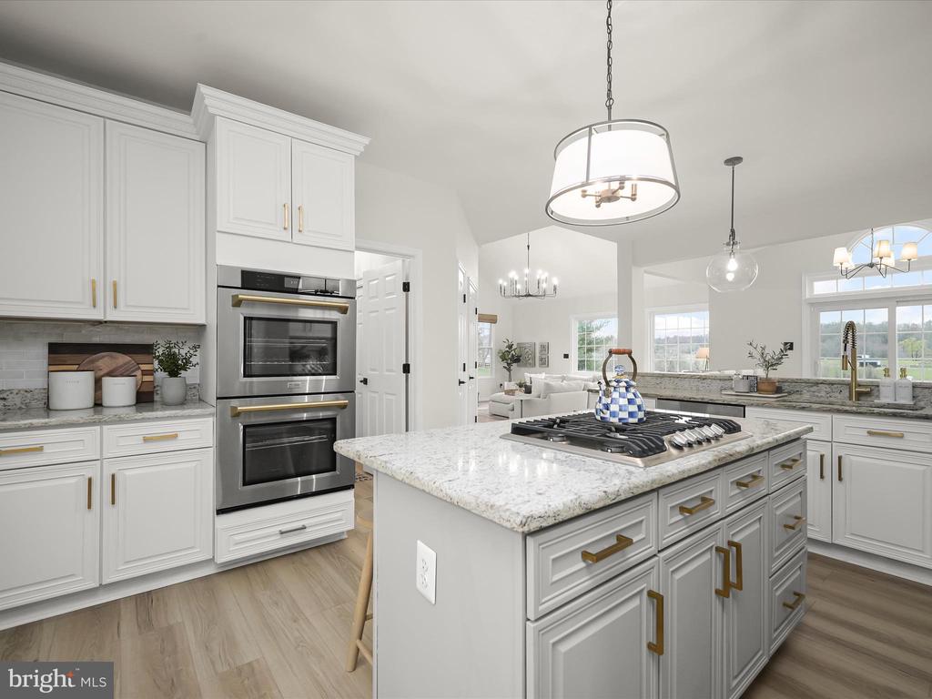 Bright kitchen with a large cooktop island, double wall oven, and white cabinetry with brass hardware.