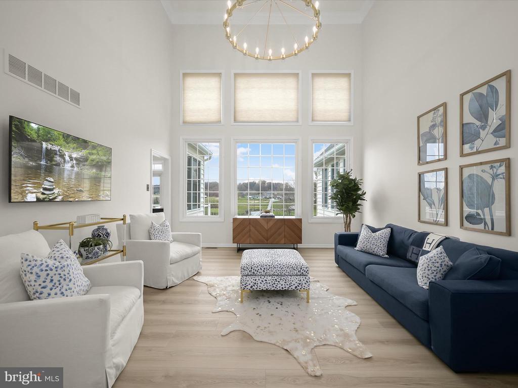 Staged living room with a high ceiling, tall windows, and a navy sofa opposite white armchairs.