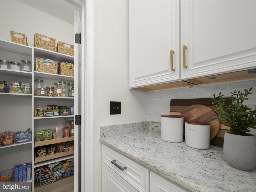 Kitchen pantry with stocked open shelves beside white cabinets and a veined stone countertop.
