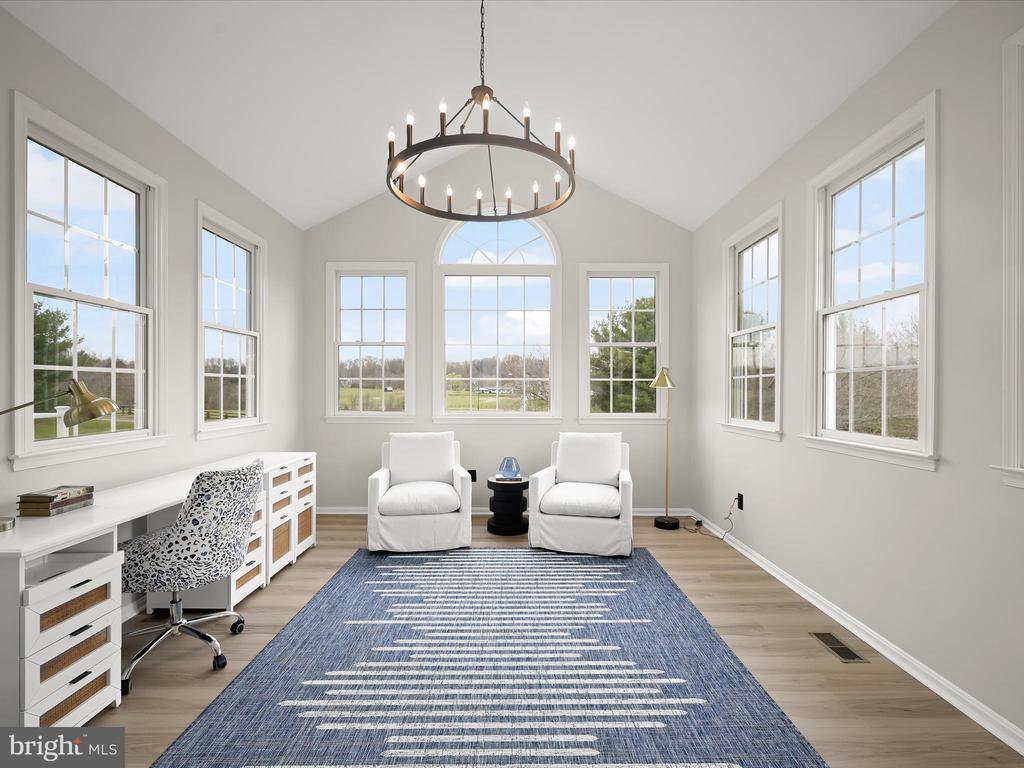 Bright home office with a white desk, two armchairs, blue rug, and large windows overlooking fields.