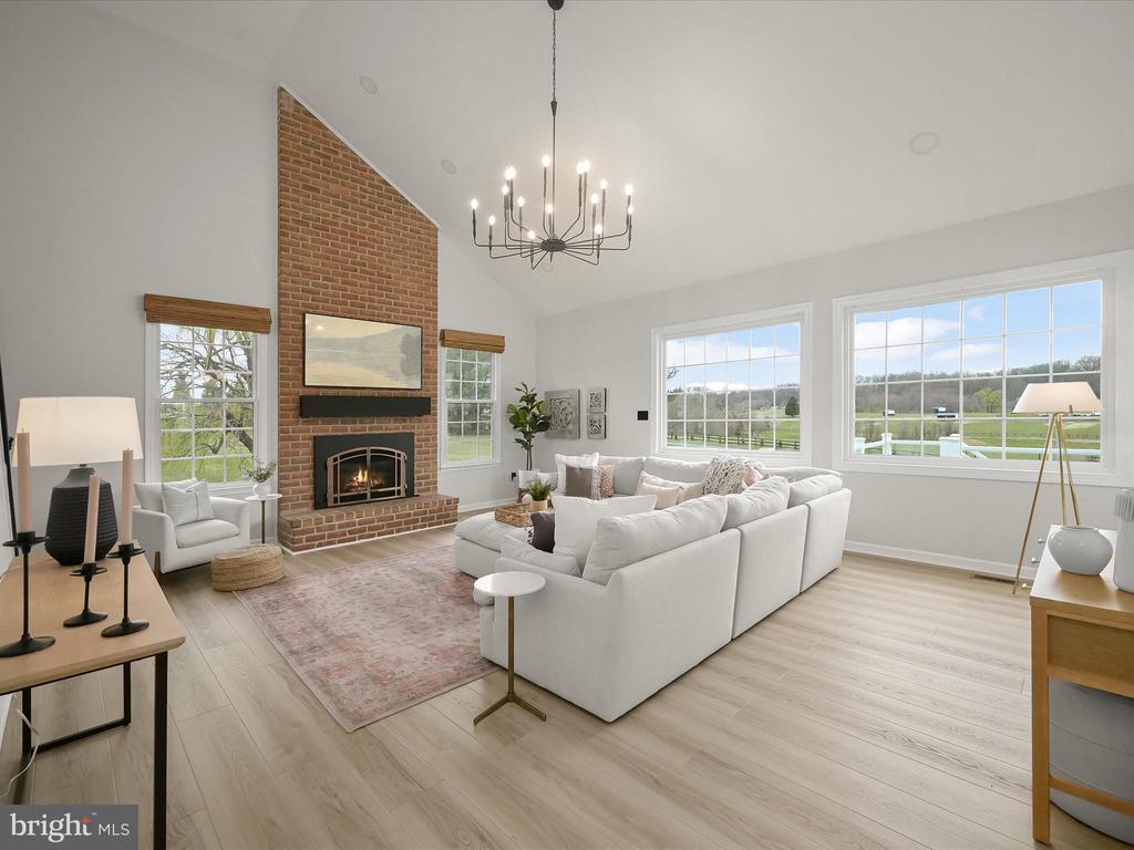 Living room with a tall brick fireplace, white sectional, and large windows overlooking open fields.