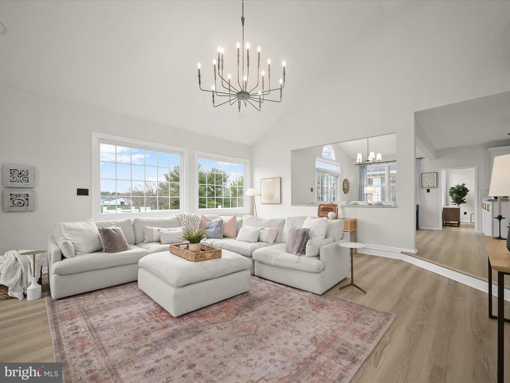 Staged living room with a white sectional, tall windows, vaulted ceiling, and modern chandelier.