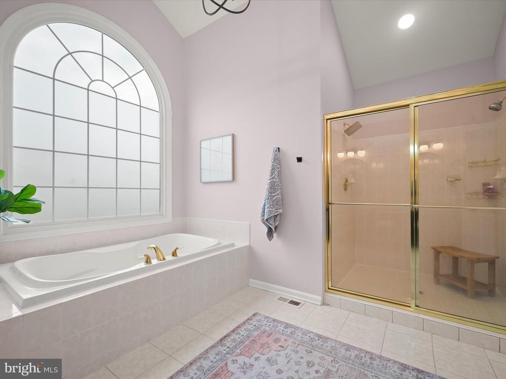 Bathroom with a soaking tub beneath an arched window and a gold-framed glass shower.