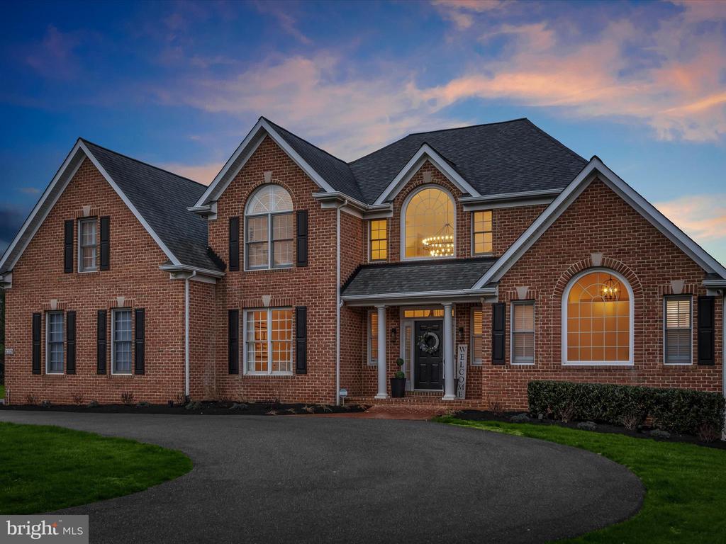 Two-story brick house with arched windows and a curved driveway at dusk.