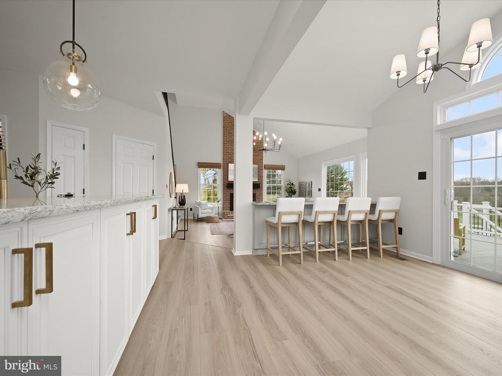 Open kitchen and dining area with white cabinetry, four island stools, and a brick fireplace beyond.