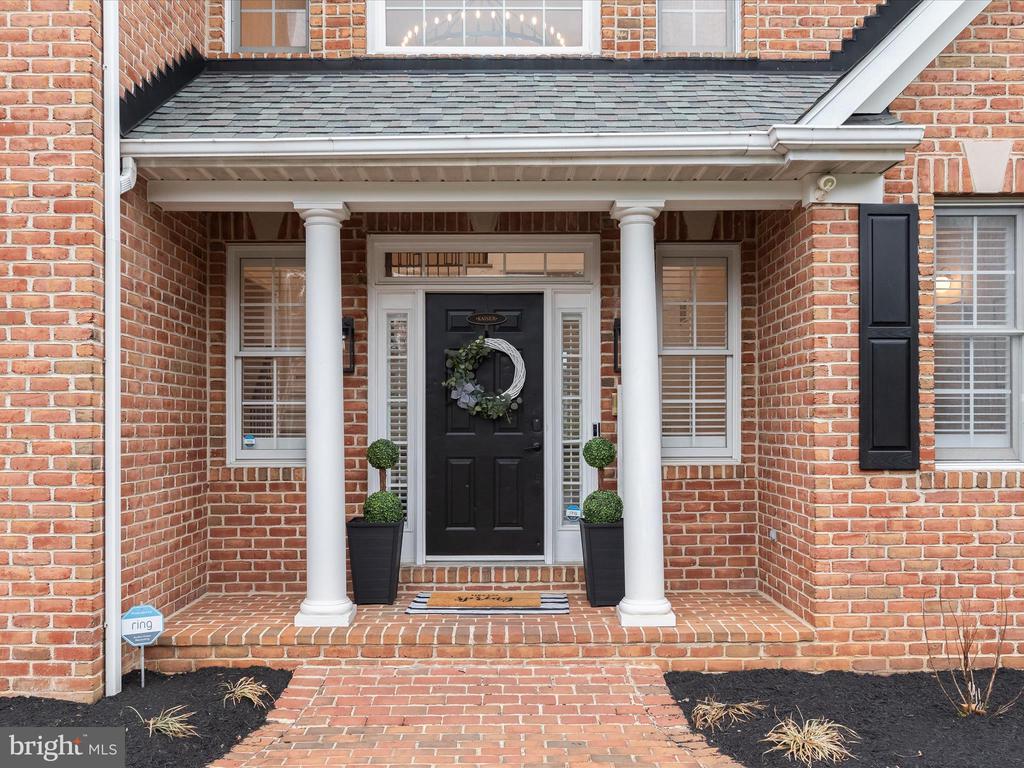 Red-brick home entrance with white columns, a black front door, and a brick walkway.