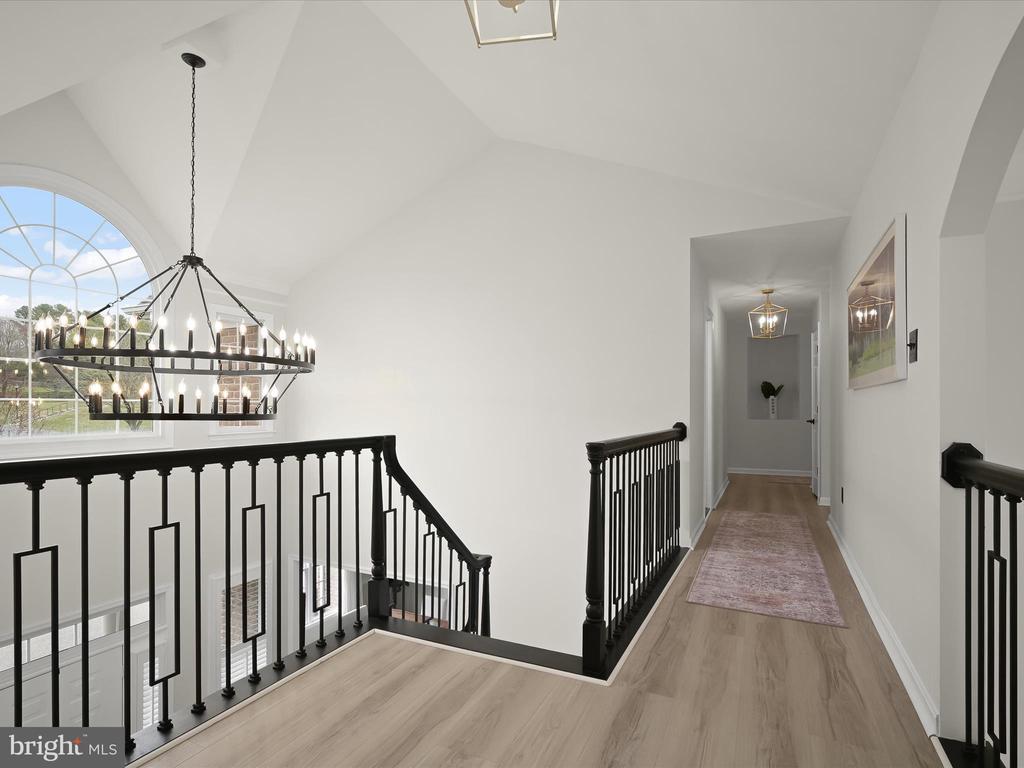 Upstairs landing with black railings, a large chandelier, and a hallway with a runner rug.