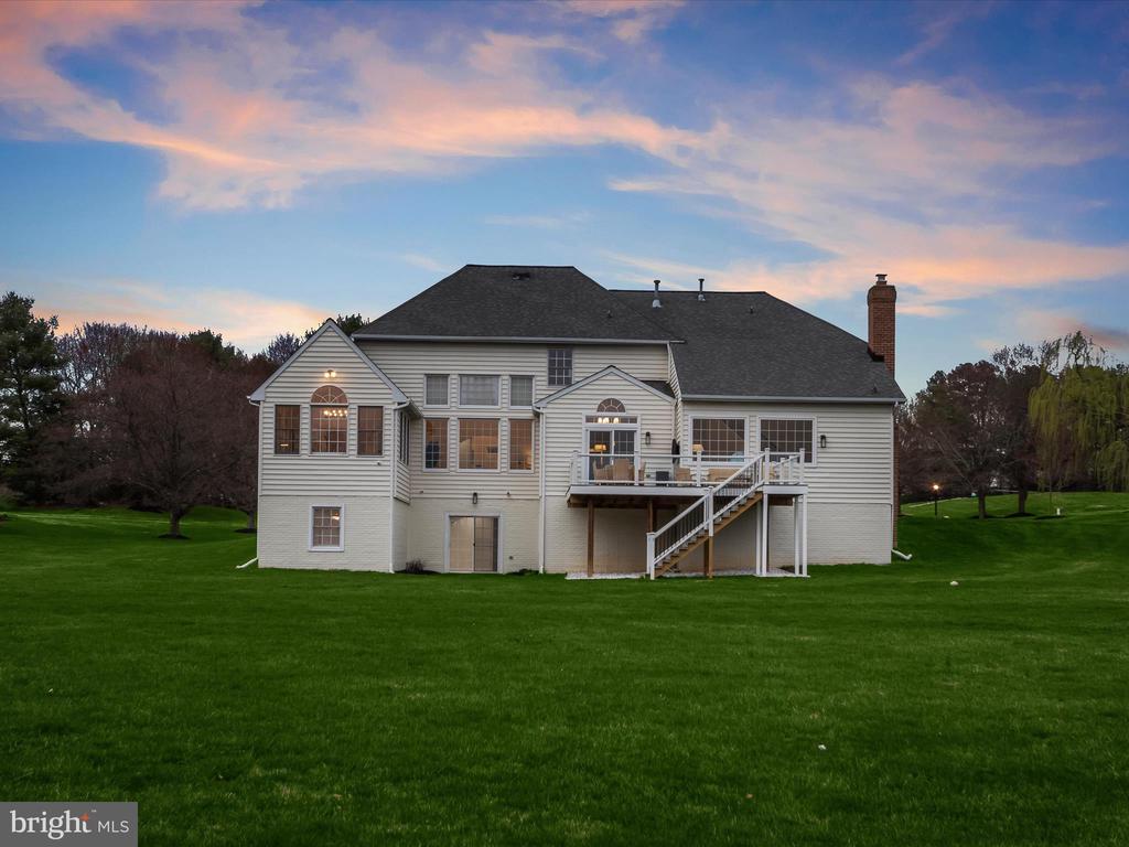 Rear exterior of a two-story home with a raised deck and broad green lawn at dusk.