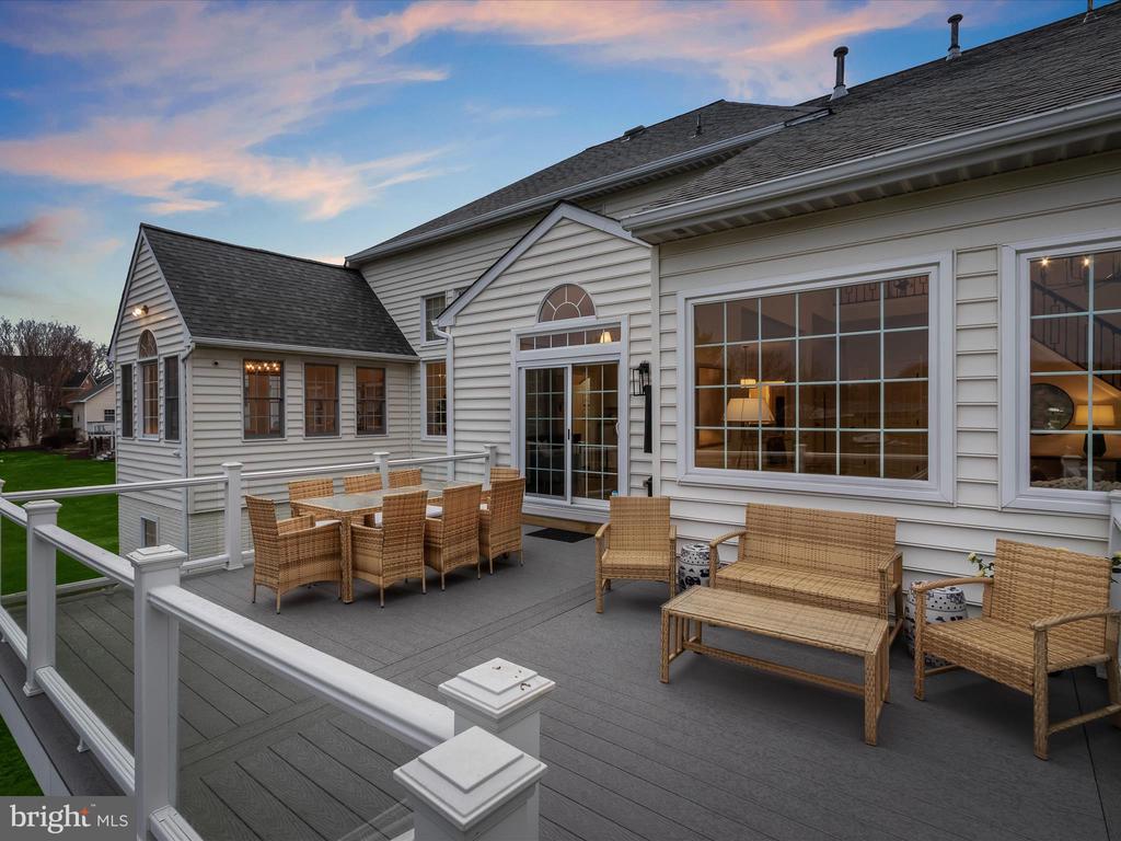 Spacious deck with wicker dining and lounge furniture beside a white-sided house at dusk.
