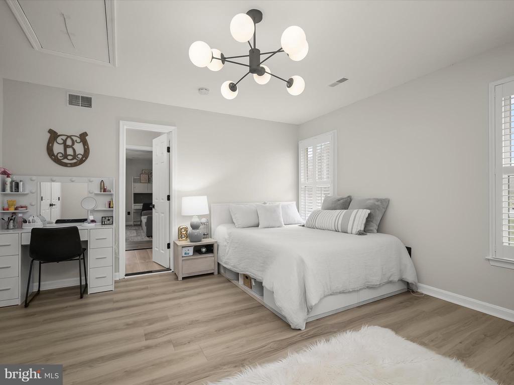 Furnished bedroom with a large white bed, vanity desk, shuttered windows, and globe chandelier.