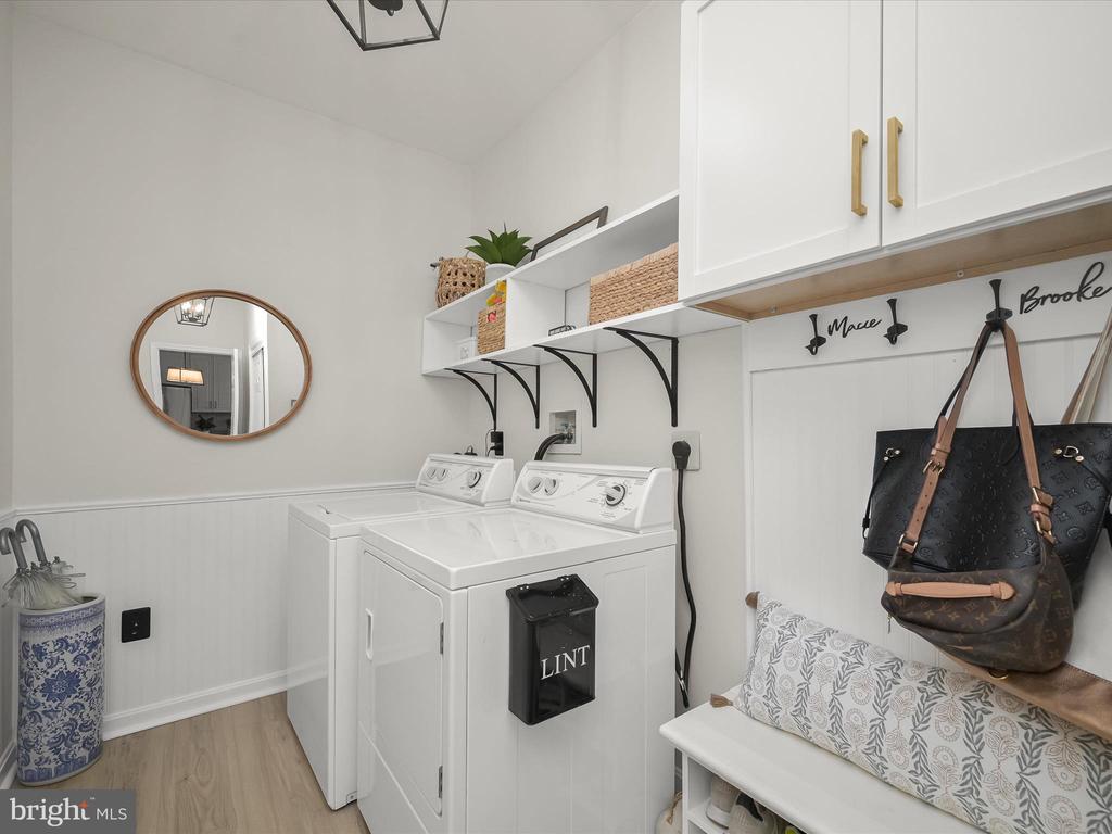 Laundry room with white washer and dryer, wall shelves, handbag hooks, and a patterned bench cushion.