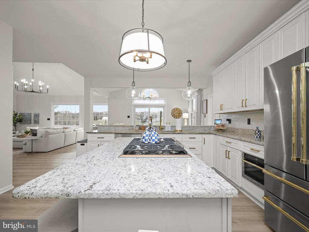 Open kitchen with a granite island, gas cooktop, white cabinetry, and stainless steel appliances.