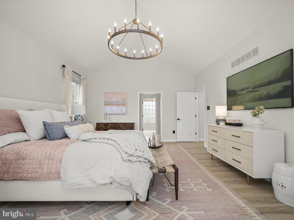 Staged bedroom with blush and white bedding, a circular chandelier, and large green wall art.