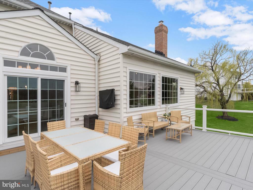 Furnished deck with wicker dining and lounge sets beside a white-sided home.