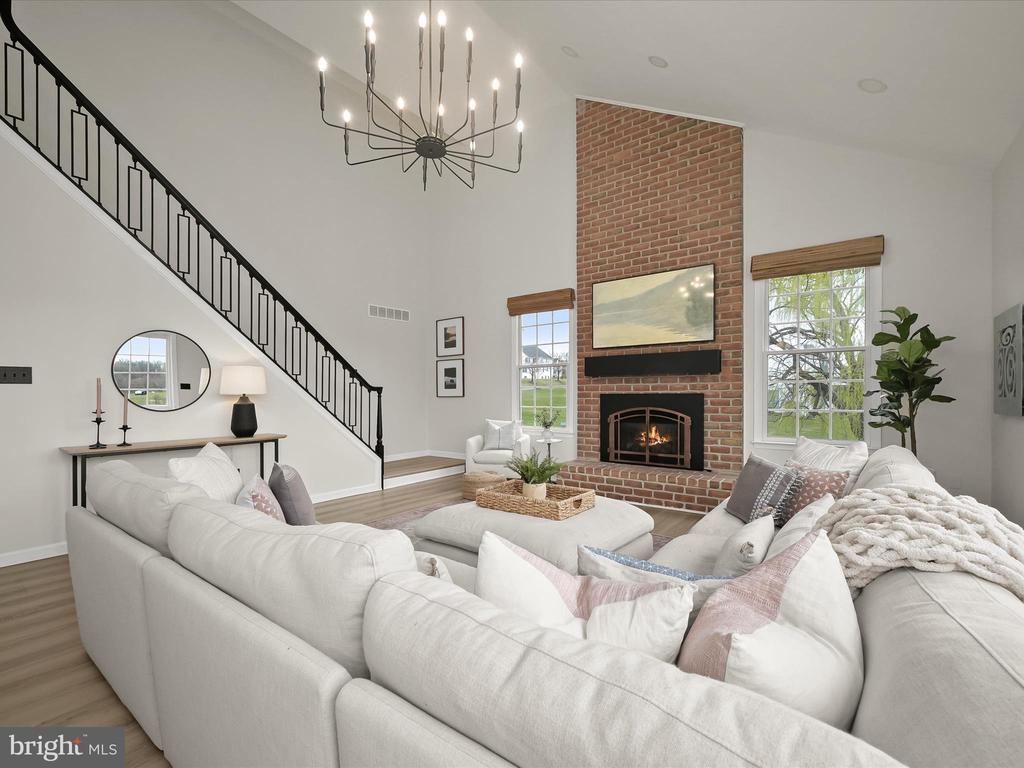 Staged living room with a brick fireplace, black-railed staircase, and large white sectional sofa.