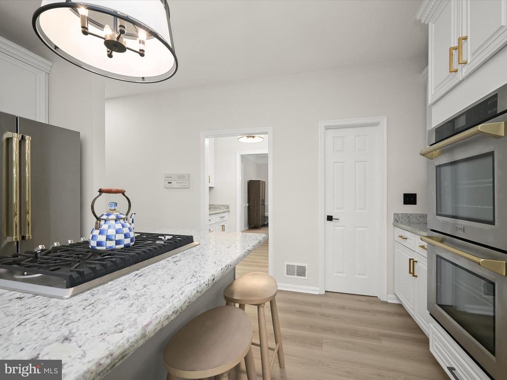 Bright kitchen with white cabinetry, stone counters, gas cooktop, and built-in double ovens.