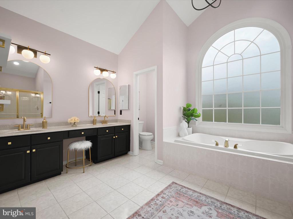 Bathroom with a soaking tub beneath an arched window and a black double vanity with gold fixtures.