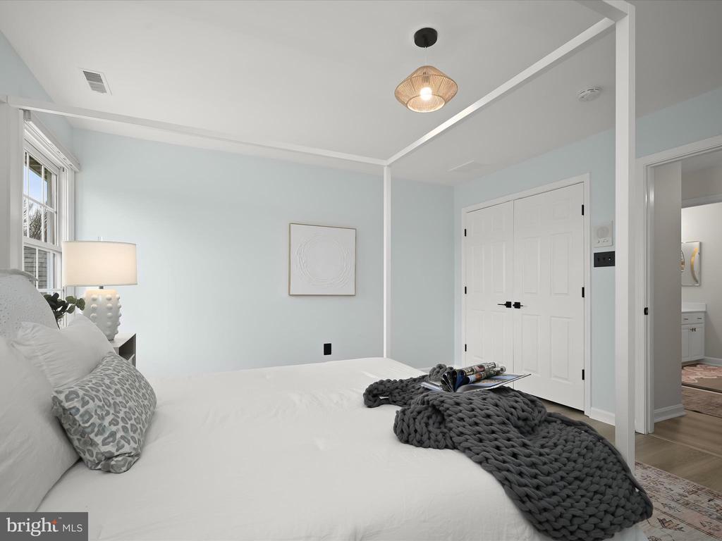 Staged bedroom with a white bed, pale blue walls, and a chunky gray knit throw.