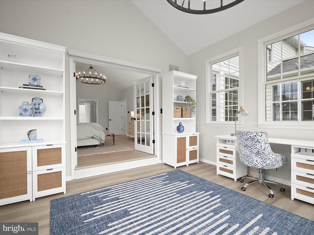 Bright home office with white built-ins, a blue rug, and French doors opening to a bedroom.