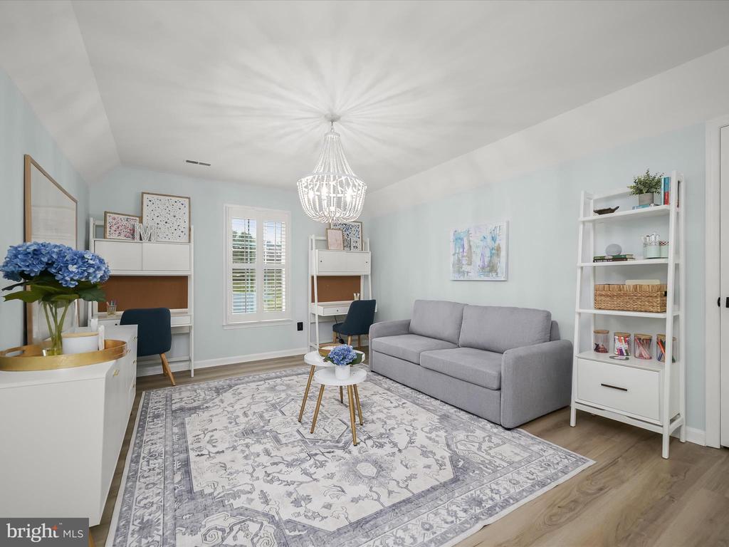 Staged home office with a gray sofa, two desks, and a large patterned rug.