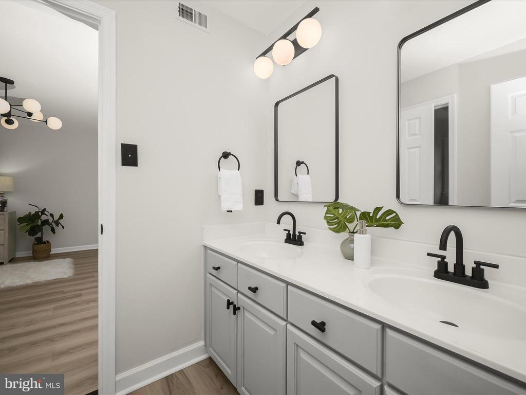Bathroom with a double vanity, gray cabinets, matte black fixtures, and two framed mirrors.